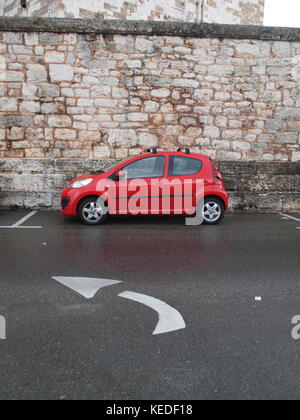 Bermuda dockyard street scene im Regen mit einem roten Auto gegen alte steinerne Mauer geparkt, weiß direktionale Straße Kennzeichnung Stockfoto
