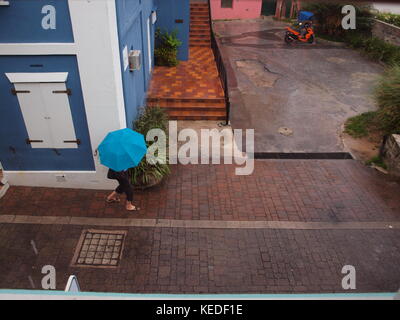 Der Water Street in St. George, Bermuda auf einem drizzily bewölkten Tag mit einer Frau unter einem blauen Regenschirm. Stockfoto