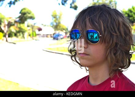 Junge Teenager männlichen trägt blaue Sonnenbrille Kopf gegen suburban Hintergrund gedreht. Stockfoto