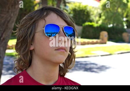 Junge Teenager männlichen trägt blaue Sonnenbrille Kopf gegen suburban Hintergrund gedreht. Stockfoto