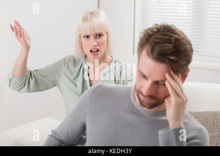 Unglückliche Frau sitzt auf einem Sofa zu schreien die frustrierter Mann Stockfoto