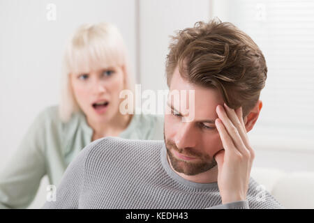 Unglückliche Frau sitzt auf einem Sofa zu schreien die frustrierter Mann Stockfoto