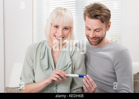 Glückliches Paar auf dem Sofa halten Schwangerschaft Tester zu Hause sitzen Stockfoto