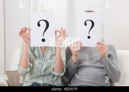 Paar sitzt auf einem Sofa holding Fragezeichen Zeichen vor Gesicht Stockfoto