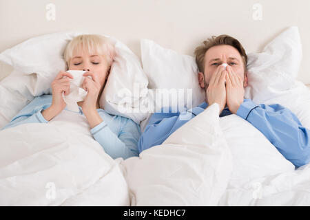 Junges Paar blasen Ihre Nase, während zu Hause im Bett liegend Stockfoto