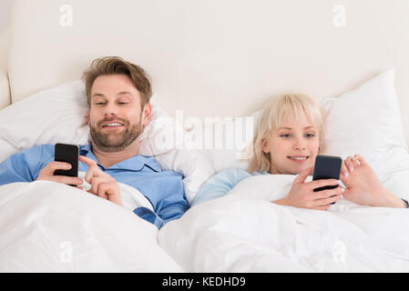 Junge glückliches Paar mit Handys beim Liegen auf dem Bett zu Hause. Stockfoto