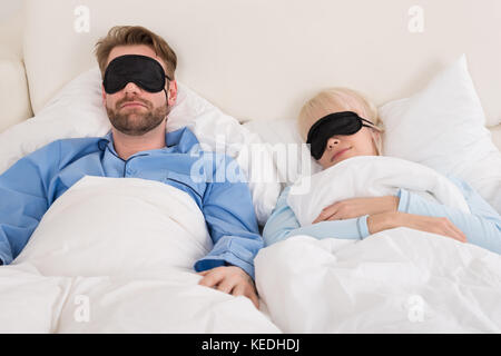 Junges Paar bequem schlafen auf Bett mit Augenmaske Stockfoto