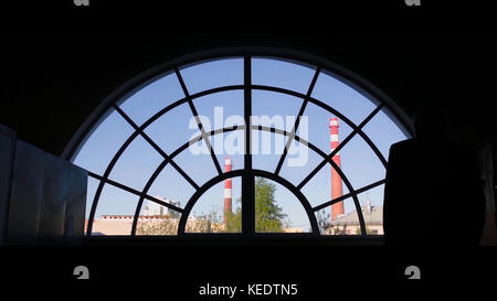 Alter Mann am Fenster. Rückansicht des alten Mannes, der zum runden Fenster kommt Stockfoto