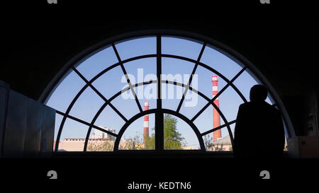 Alter Mann am Fenster. Rückansicht des alten Mannes, der zum runden Fenster kommt Stockfoto