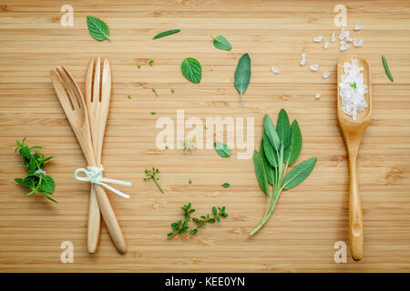 Aromatische Kräuter und Gewürze grüne Minze, Fenchel, Oregano, Salbei, Rosmarin, Zitrone, Thymian und Pfefferminze mit Gabel und Meersalz in der Löffel auf Bambus Stockfoto