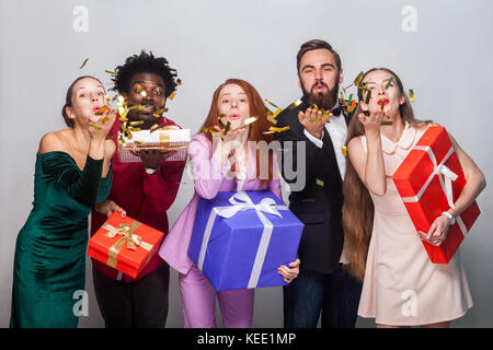 Glück Freunde feiern das neue Jahr. drop out gold Konfetti an Kamera und halten viele Geschenkbox. Studio shot auf grauem Hintergrund Stockfoto