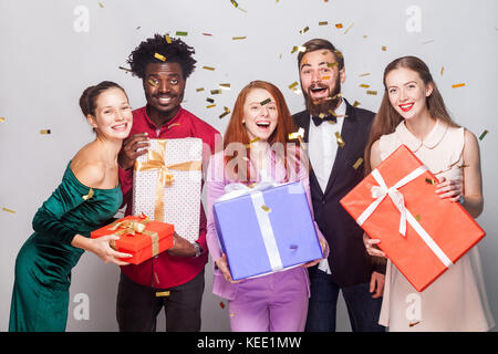 Attraktive Menschen feiern das neue Jahr. halten viele Geschenk Box, Kamera und toothy Lächeln. Studio shot auf grauem Hintergrund Stockfoto