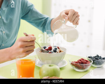 Frau mit einem gesunden Frühstück zu Hause, sie gießt Milch in eine Schüssel geben, gesunde Ernährung Konzept Stockfoto