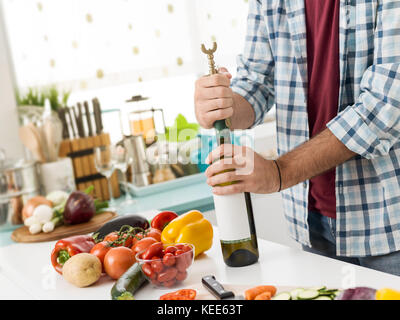 Man öffnet eine Flasche Wein in der Küche, er ist mit einem Korkenzieher Stockfoto
