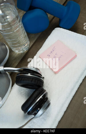 Schuhe, Kopfhörer, Wasserflasche und Handtuch, Kurzhantel- und stick Notes auf hölzernen Tisch Stockfoto