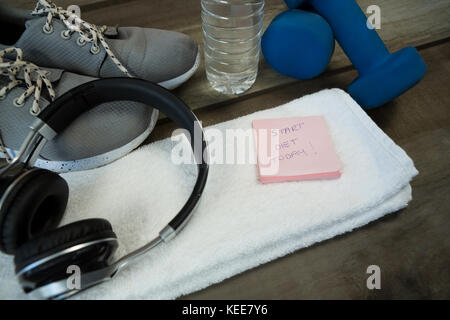 Schuhe, Kopfhörer, Wasserflasche und Handtuch, Kurzhantel- und stick Notes auf hölzernen Tisch Stockfoto