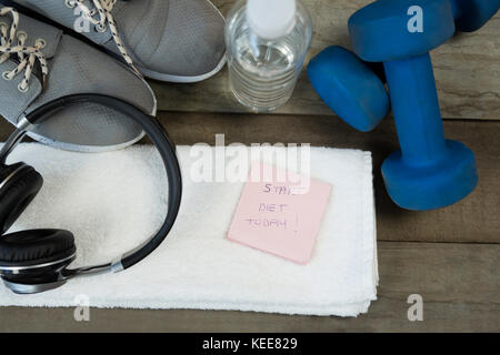 Schuhe, Kopfhörer, Wasserflasche und Handtuch, Kurzhantel- und stick Notes auf hölzernen Tisch Stockfoto