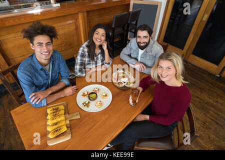 Gerne Freunde sitzen zusammen mit baby Mais, Snacks und Bier am Tisch in der Bar Stockfoto