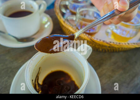 Hand hinzufügen mit einem Löffel eine Kopi Luwak Kaffee von der Plantage in Bali, Indonesien, auf hölzernen Hintergrund Stockfoto