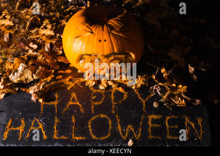 Einen geschnitzten Kürbis schaut zu erbrechen die Phrase happy halloween werden aus der Zellstoff- und durch Blätter umgeben Stockfoto