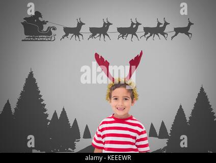 Digital composite der Junge gegen den grauen Hintergrund mit Rentier Geweih auf dem Kopf und Santa fliegen im Schlitten Stockfoto
