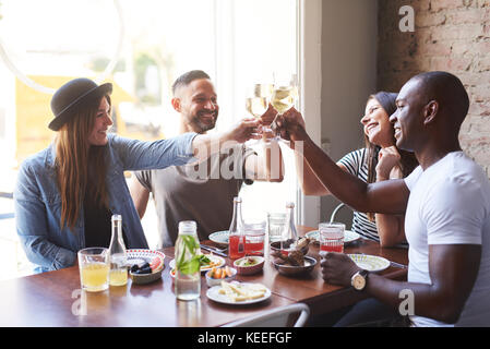 Eine Gruppe von vier jungen Menschen lachen und Sitzen am Tisch im Restaurant und klirren Gläser mit Wein. Stockfoto
