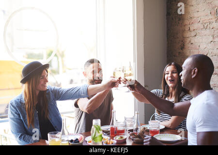 Gruppe von verschiedenen männlichen und weiblichen jungen Erwachsenen etwas Feiern mit Wein am Tisch im Restaurant Stockfoto