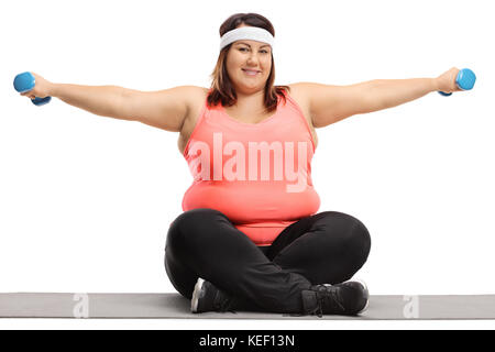 Übergewichtige Frau auf einem trainingsmatte Trainieren mit kleinen Hanteln auf weißem Hintergrund sitzt Stockfoto