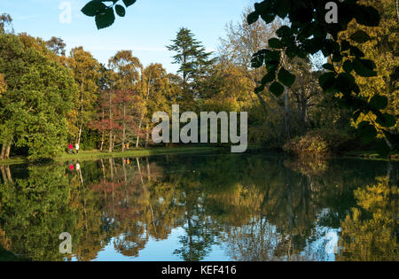 Gosford Estate, East Lothian, Schottland, 20. Oktober 2017. Wässrige Reflexionen während die niedrige Nachmittagssonne den künstlichen See im Gosford Anwesen erleuchtet und eine Familie einen Herbstspaziergang entlang der Seeufer genießt, reflektiert im Wasser Stockfoto