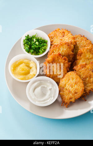 Kartoffelpuffer, latkes oder Boxty und Saucen aus Sauerrahm, Joghurt, Apfelmus und fein gehackten Frühlingszwiebeln auf einem blauen Hintergrund Stockfoto
