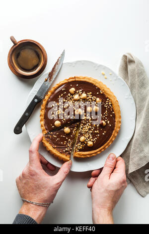 Italienische walnuss Kuchen crostata mit Schokolade und Haselnüssen. und Kaffee. menschenhänden einen Schnitt Stück Stockfoto