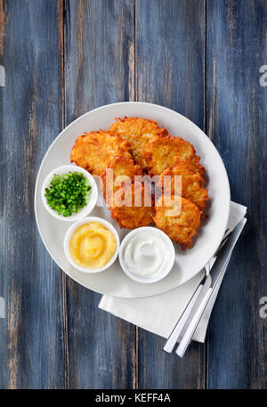 Kartoffelpuffer, latkes oder Boxty und Saucen aus Sauerrahm, Joghurt, Apfelmus und fein gehackten Frühlingszwiebeln auf einem hölzernen Tisch der Platten Stockfoto