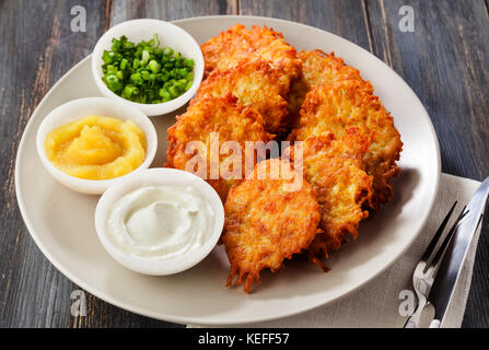 Kartoffelpuffer, latkes oder Boxty und Saucen aus Sauerrahm, Joghurt, Apfelmus und fein gehackten Frühlingszwiebeln auf einem hölzernen Tisch der Platten Stockfoto