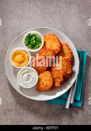 Kartoffelpuffer, latkes oder Boxty und Saucen aus Sauerrahm, Joghurt, Apfelmus und fein gehackten Frühlingszwiebeln auf grauem Stein Hintergrund Stockfoto