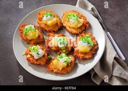 Kartoffelpuffer, latkes oder Boxty und Saucen aus Sauerrahm, Joghurt, Apfelmus und fein gehackten Frühlingszwiebeln auf grauem Stein Hintergrund Stockfoto