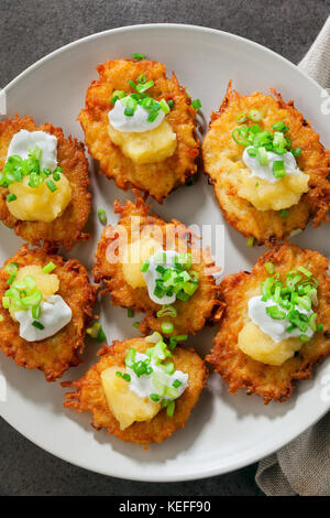 Kartoffelpuffer, latkes oder Boxty und Saucen aus Sauerrahm, Joghurt, Apfelmus und fein gehackten Frühlingszwiebeln auf grauem Stein Hintergrund Stockfoto