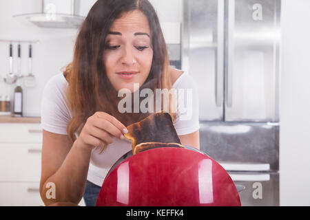 Junge Frau, die Scheibe der Burnt Toast aus der Toaster in der Küche Stockfoto