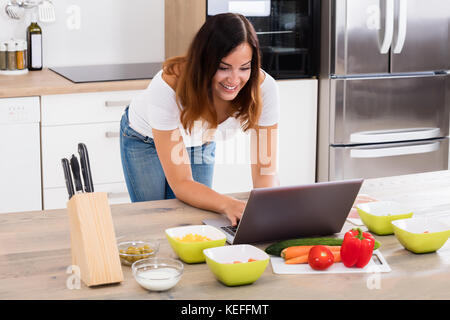 Lächelnde Frau mit Laptop für Küche leckere Los in der Küche Stockfoto