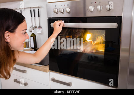 Junge Frau rösten Hähnchenfleisch in Küche Backofen Stockfoto