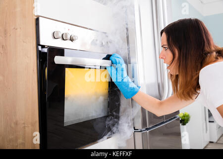 Junge Frau von Rauch aus Backofen in der Küche geschockt Stockfoto