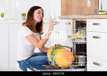 Junge Frau unter Glas von Spülmaschine in der Küche Stockfoto