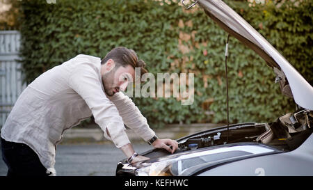 Hübscher junger Mann versucht, einen Automotor, reparieren Blick in offene Motorhaube Stockfoto