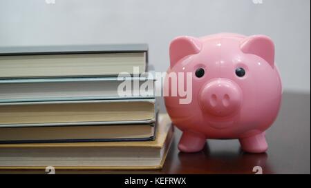 Pink Piggy Bank steht neben einem Stapel Lehrbücher Stockfoto