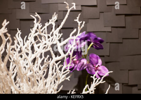 Handgefertigte künstliche weiss verschneiten Zweig mit einem lila Blumen auf einem dunklen Hintergrund in Form von Fliesen Stockfoto