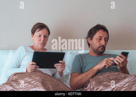 Paar, Mann und Frau im Schlafzimmer über elektronische Geräte gelangweilt Stockfoto