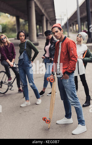 Jungen gutaussehenden Mann skateboard Holding mit unscharfen Freunde auf Hintergrund Stockfoto