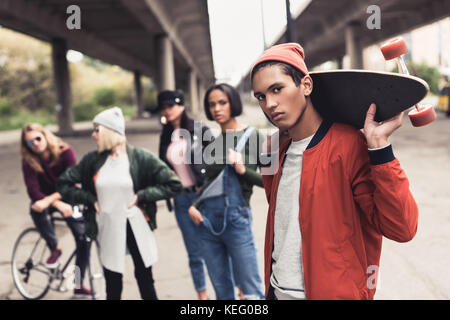 Jungen gutaussehenden Mann skateboard Holding mit unscharfen Freunde auf Hintergrund Stockfoto
