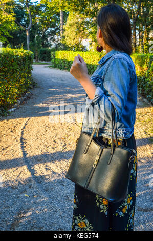 Ein Porträt einer jungen Frau, trug einen geblümten Kleid und einer Jeansjacke, die eine schwarze Handtasche Stockfoto