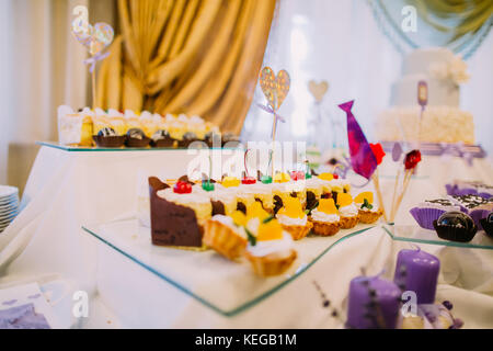 Seitliche Sicht auf das köstliche Hochzeit Cupcakes auf dem Tisch mit Kerzen geschmückt. Stockfoto