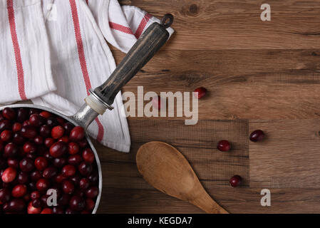 Frische Cranberries in einem Topf zum Kochen bereit. verstreut Beeren einen Löffel und Küchentuch auf dem Holz Tisch sind. Stockfoto